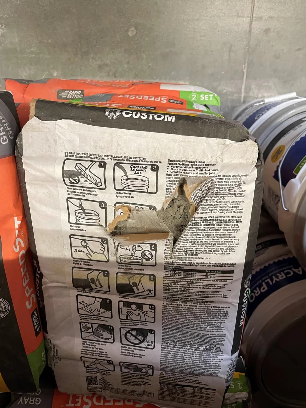 A bag of thin-set mortar with a large tear in the side, product spilling out